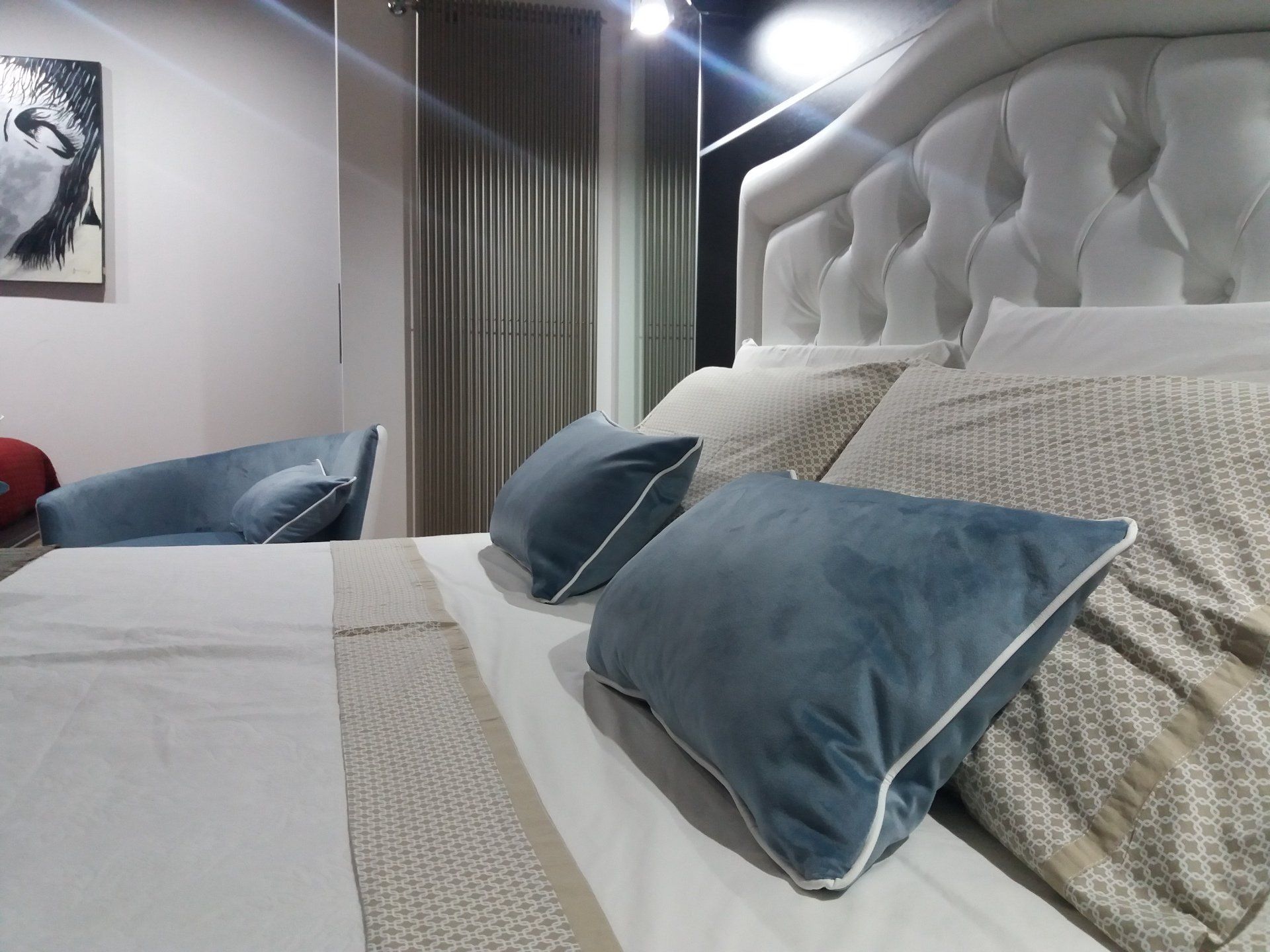 Camera da letto con una grande testiera bianca, cuscini blu e una piccola sedia blu.