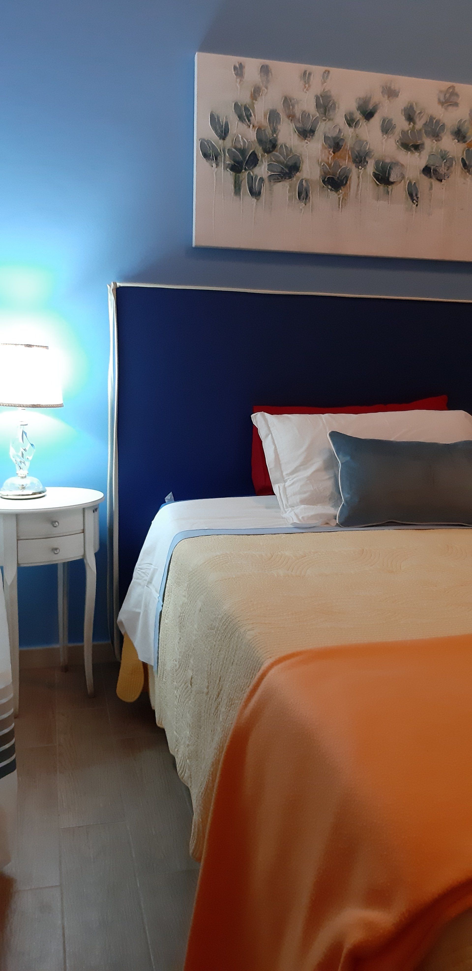 Camera da letto con pareti blu, letto con cuscini e coperta, comodino con lampada.