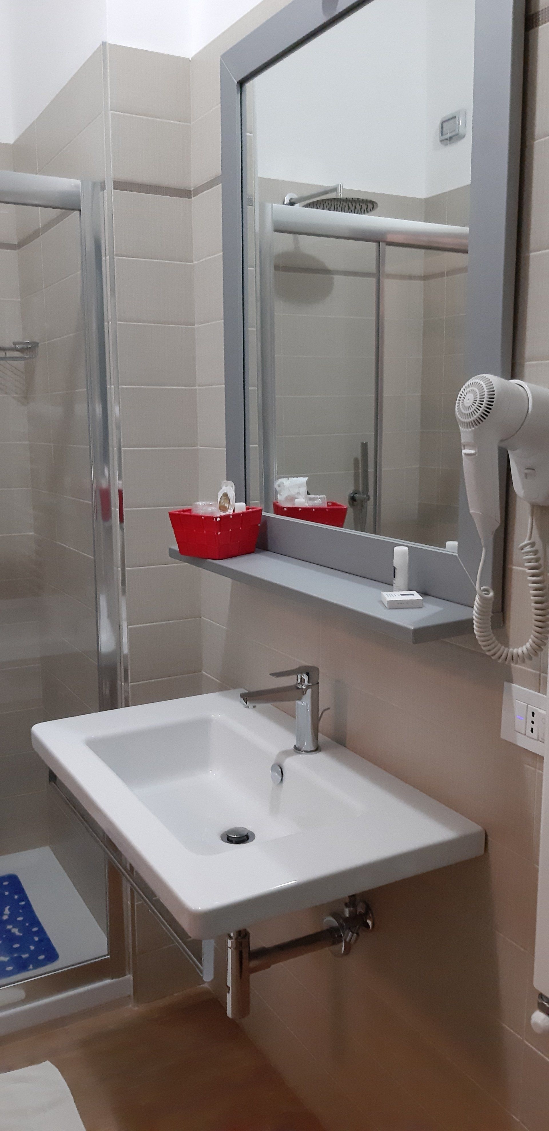 Bagno con lavabo a parete, specchio e box doccia. Include asciugacapelli e articoli da toeletta.
