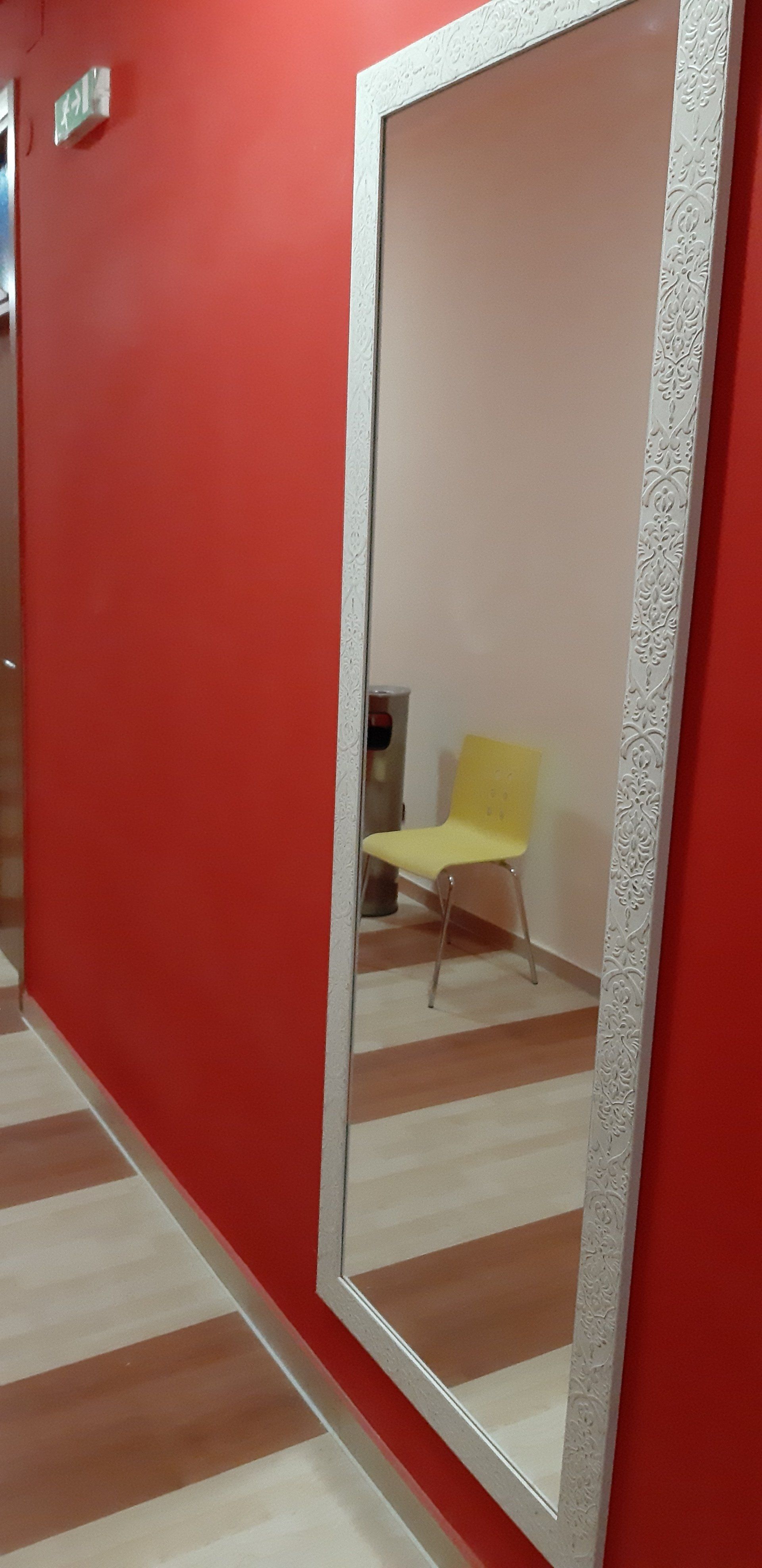 Un corridoio rosso con un grande specchio che riflette una sedia gialla e una stanza color marrone chiaro.
