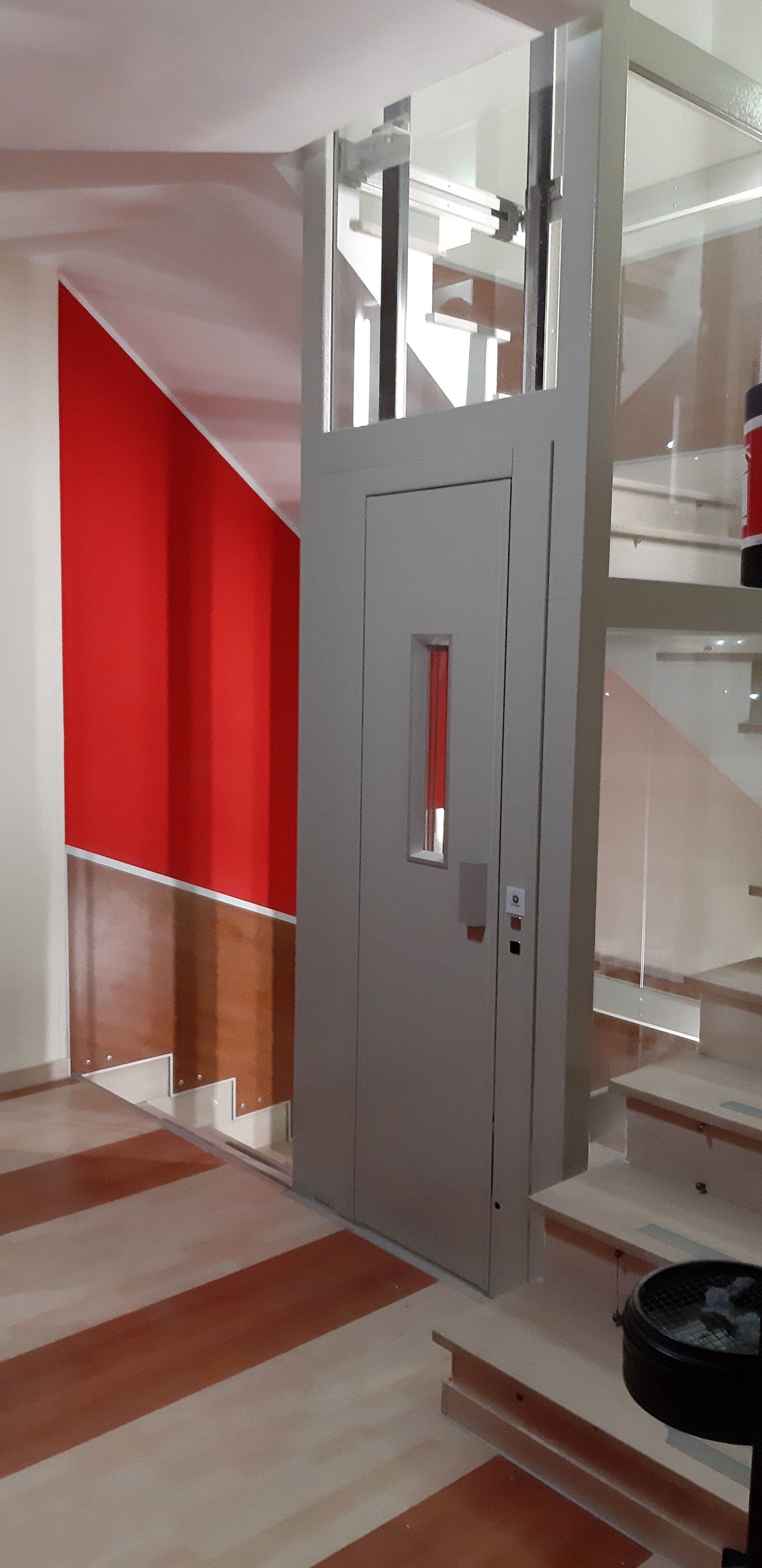 Un ascensore chiuso accanto a una scala. L'ascensore ha una porta metallica con una finestra rossa. Parete rossa e pavimento decorato.
