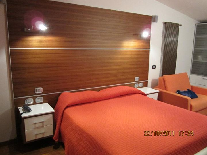 Camera d'albergo con letto, comodini e poltrona arancione. Testiera e parete in legno.
