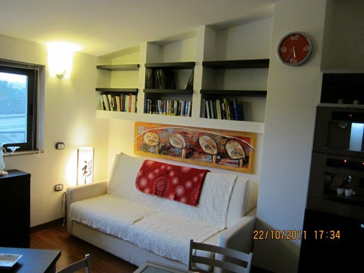 Soggiorno con divano bianco, librerie, quadri e un orologio.