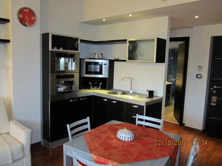 Piccola cucina con mobili neri, microonde e lavello, accanto a una zona pranzo con una tovaglia rossa.