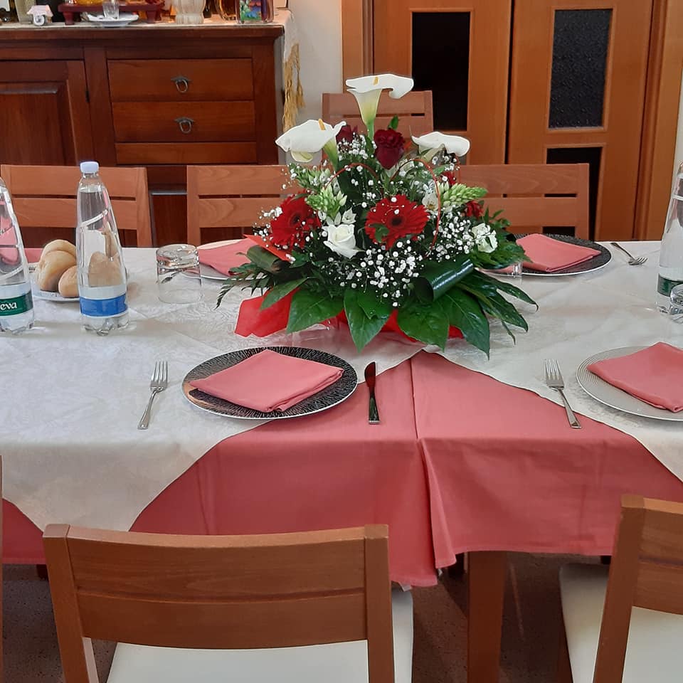 Tavolo apparecchiato per un pasto, con centrotavola floreale, piatti e bottiglie d'acqua, in una sala da pranzo.