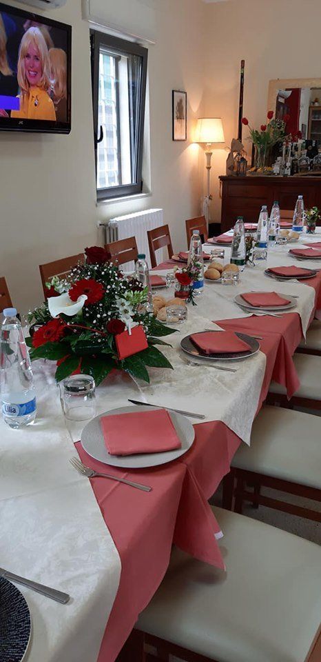 Un lungo tavolo da pranzo apparecchiato per un pasto con accenti, fiori e apparecchiature color rosa.