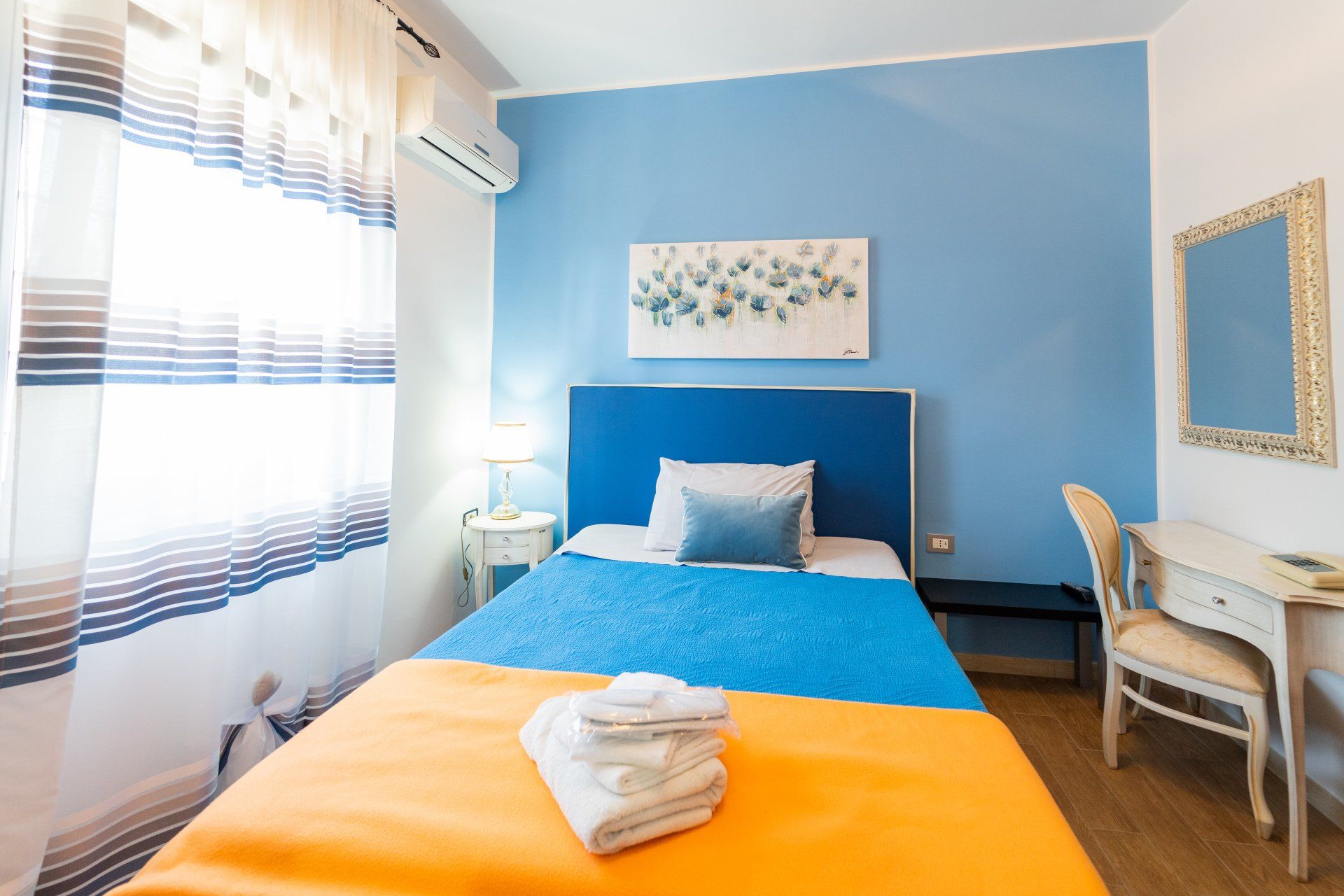 Camera da letto blu e arancione con letto singolo, scrivania e finestra.