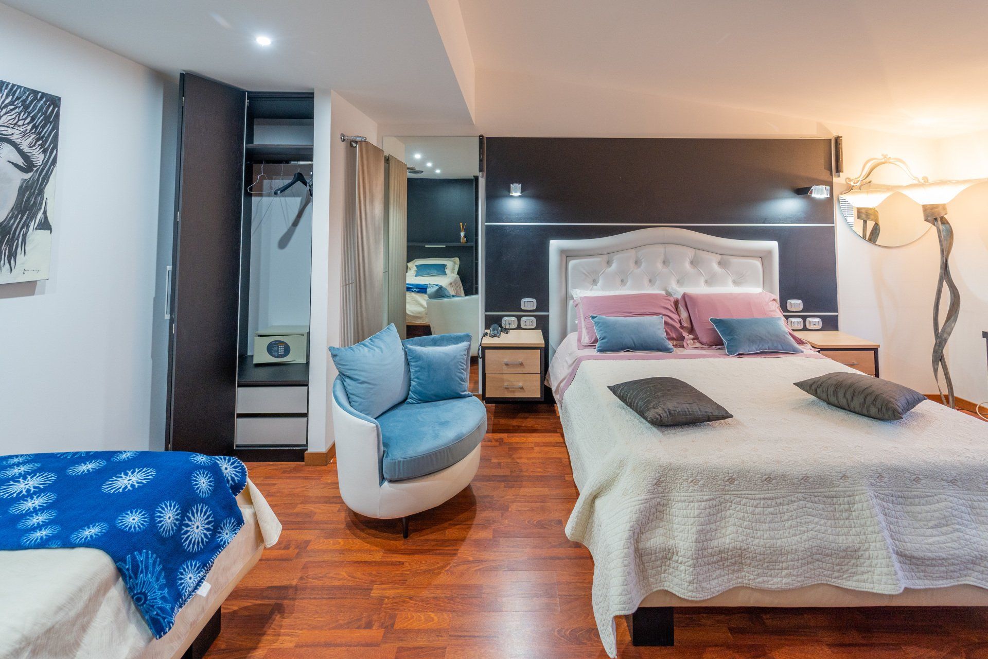 Camera da letto con letto matrimoniale, poltrona, armadio e lampada da terra. Pavimento in legno.