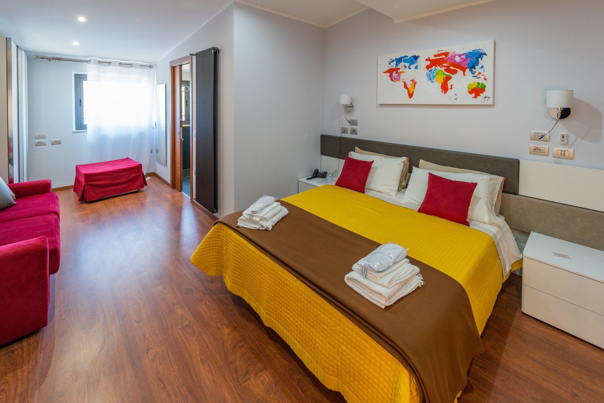 Camera d'albergo con un letto, un divano rosso e una mappa del mondo colorata.