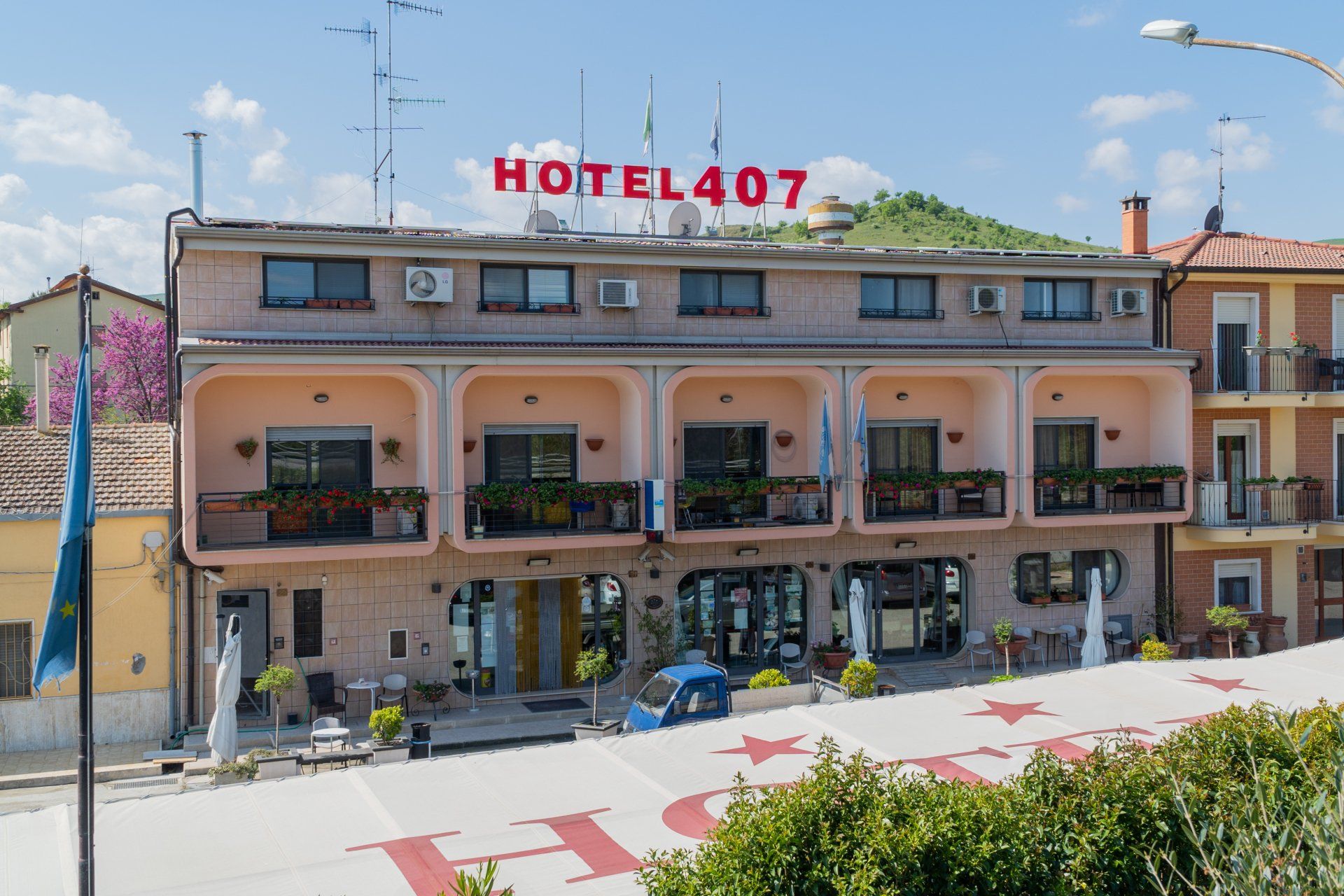 Hotel 407: un edificio di tre piani con balconi, un'insegna rossa e un'auto blu parcheggiata di fronte.