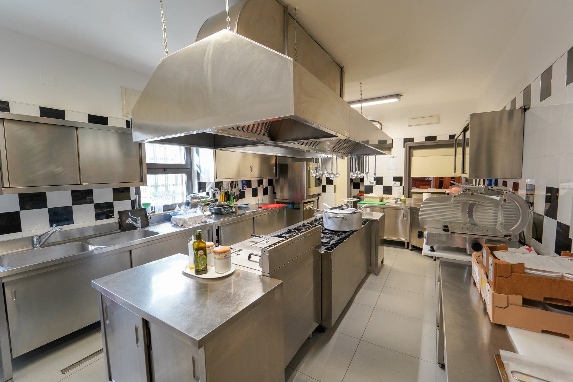 Cucina commerciale in acciaio inox con elettrodomestici e cappa aspirante.