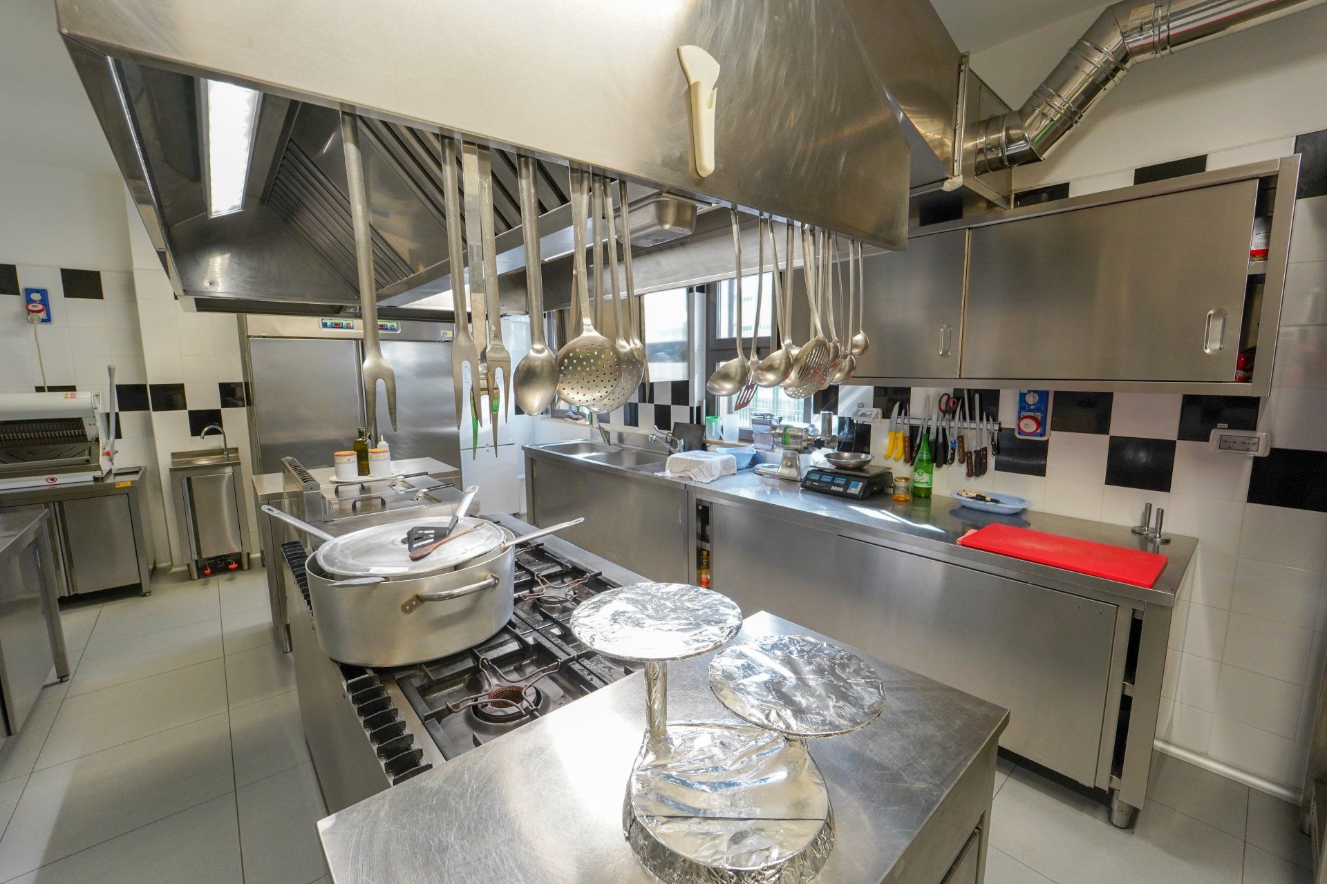 Cucina commerciale con elettrodomestici in acciaio inossidabile, pentole sui fornelli e utensili appesi.