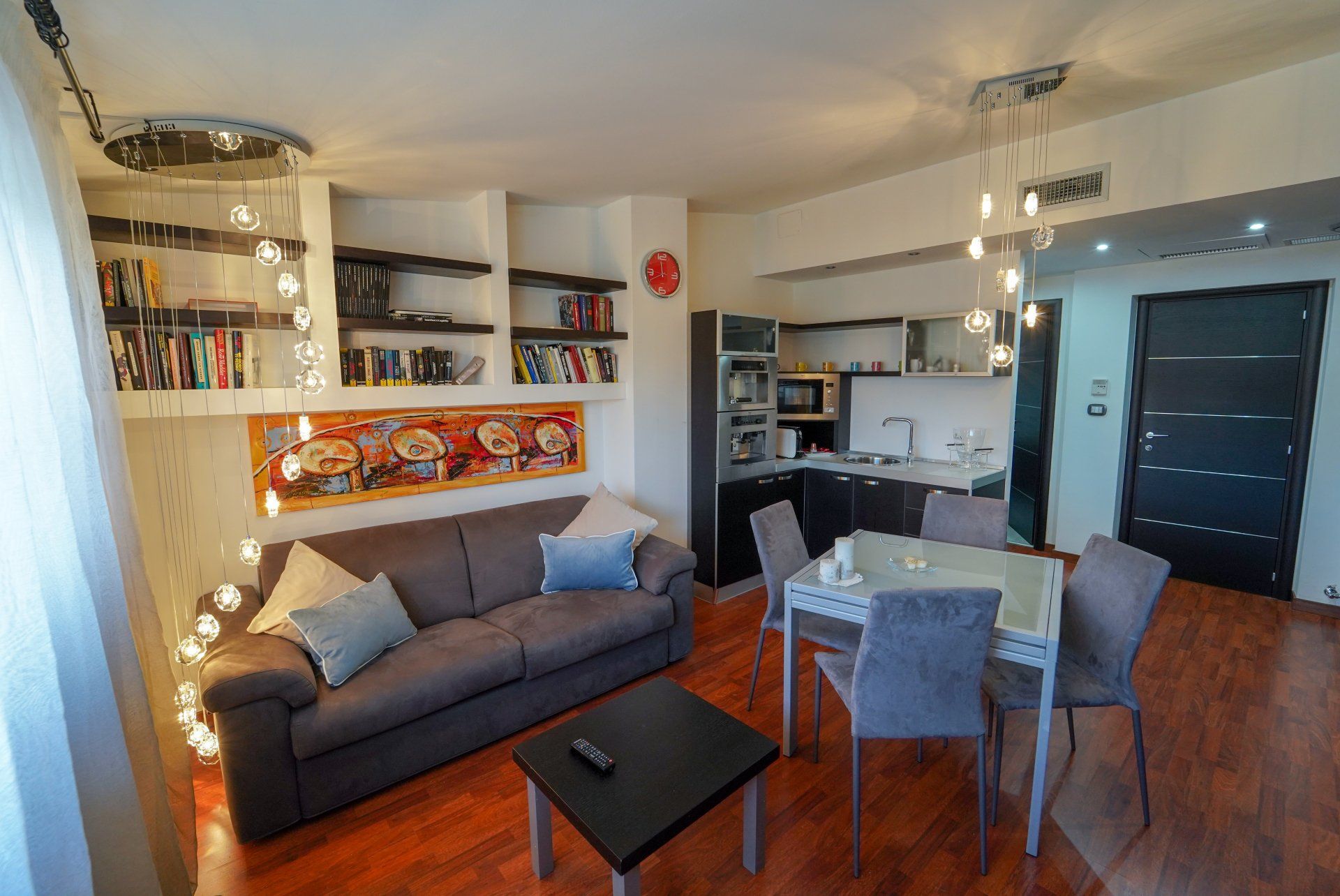 Accogliente appartamento con divano, librerie, piccola cucina, zona pranzo e pavimenti in legno scuro.