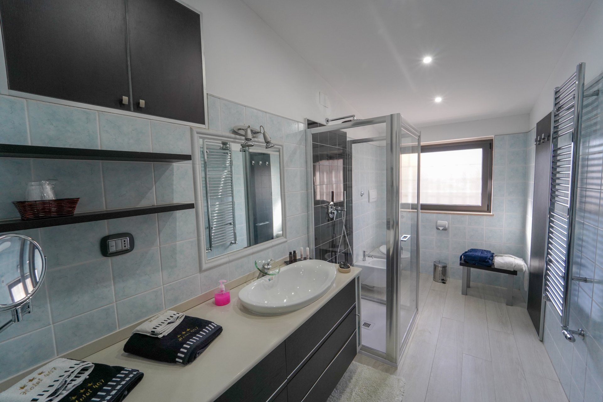 Bagno con pareti piastrellate blu, doccia, mobiletto con specchio e mobili scuri.
