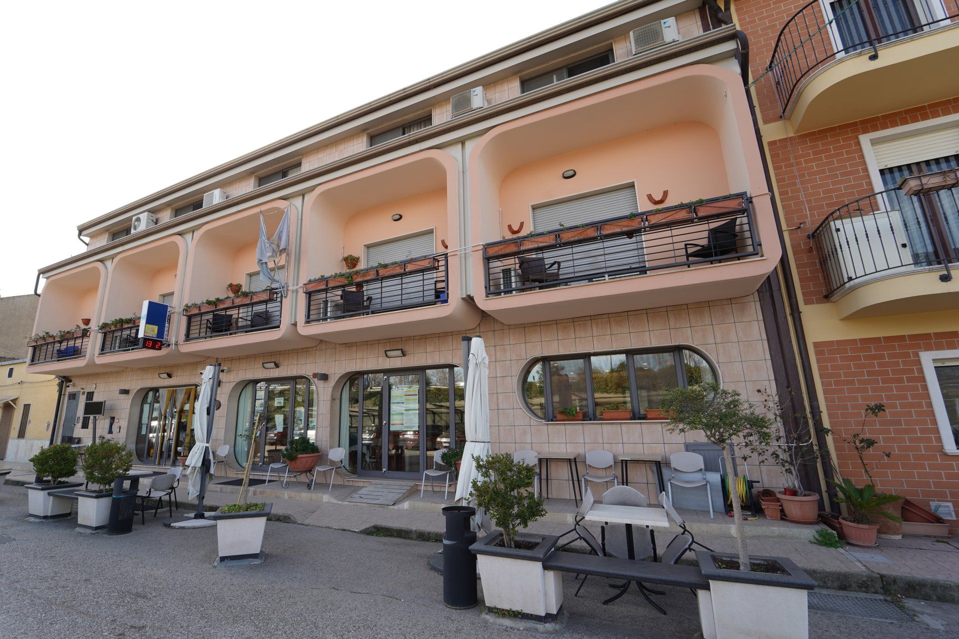 Edificio adibito a ristorante con posti a sedere all'aperto; esterno color pesca, balconi e ampie finestre.