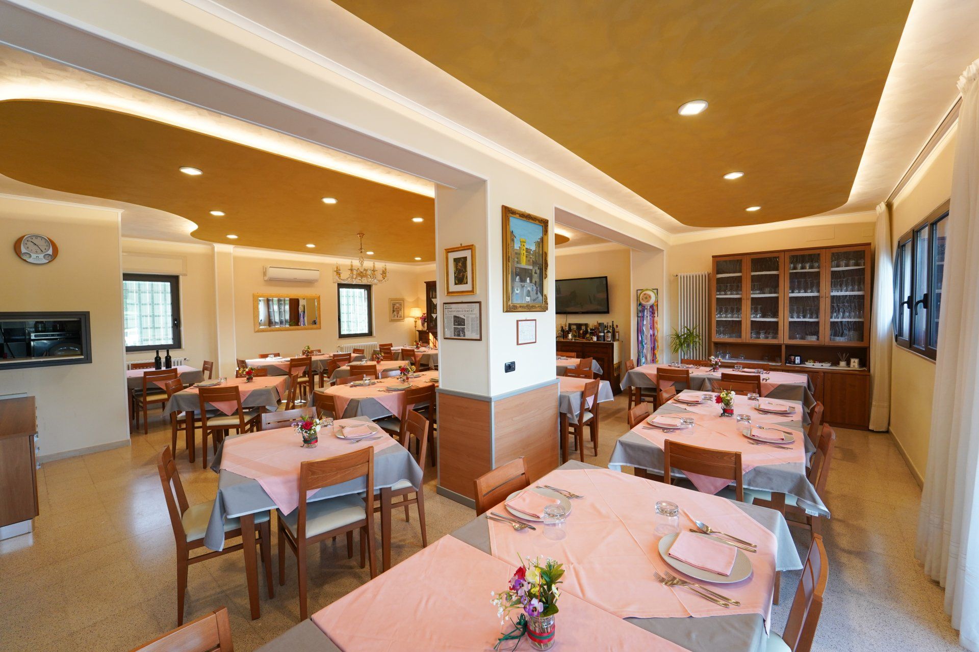 Sala da pranzo del ristorante con tavoli apparecchiati per il servizio, tovaglie rosa e soffitto dorato.