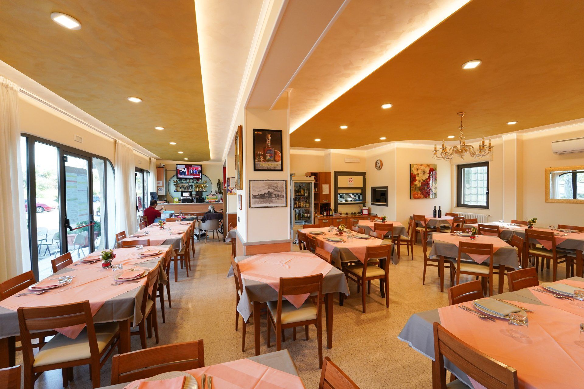 Interno del ristorante: tavoli apparecchiati con tovaglie rosa, sedie in legno, luci calde e pochi clienti.