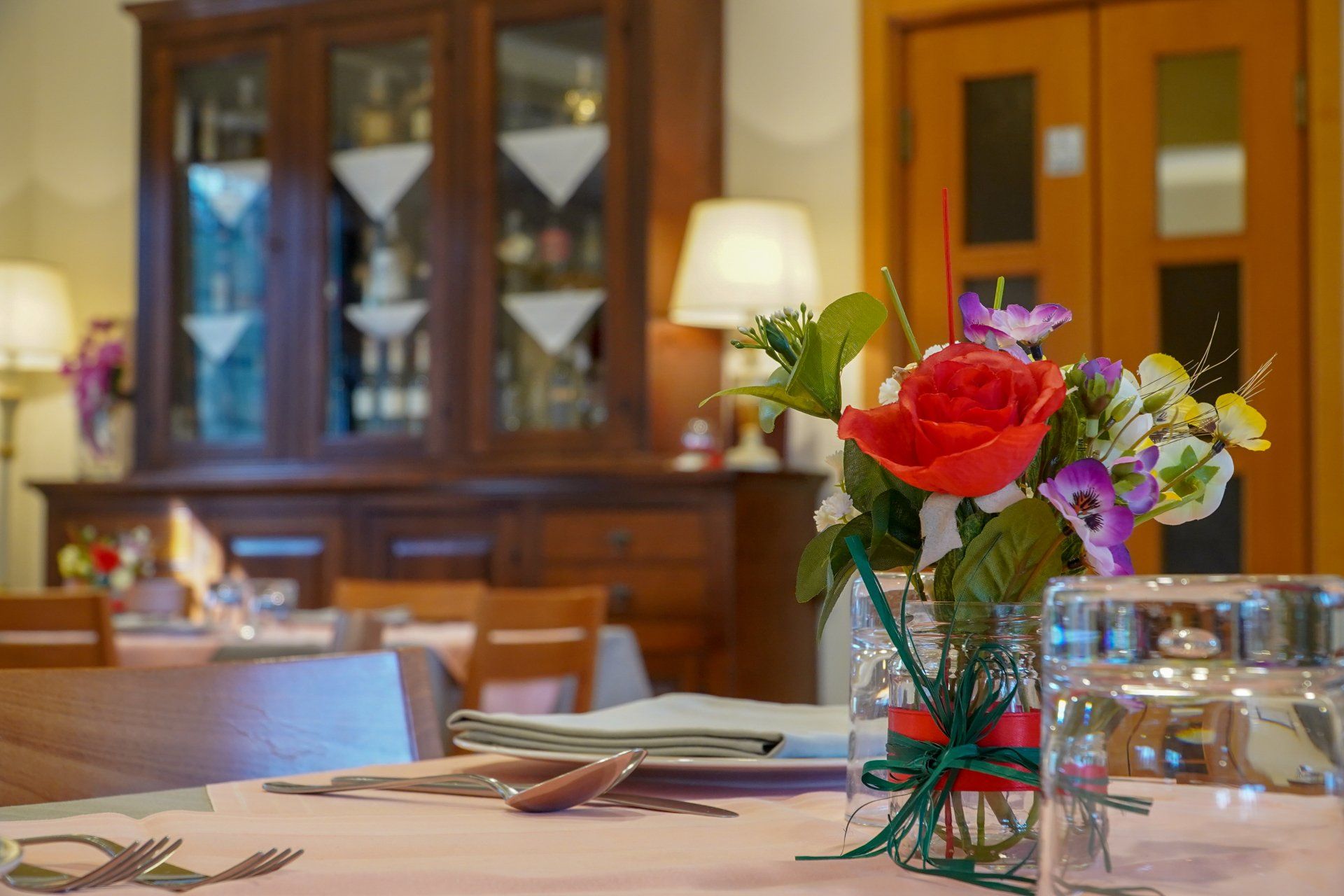 Apparecchiatura del tavolo con composizione floreale, credenza in legno e doppie porte in un ristorante.