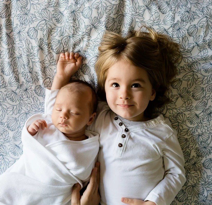 A little girl is laying next to a newborn baby on a bed.