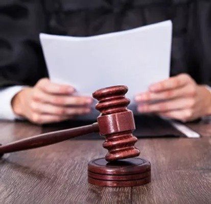 A judge is sitting at a table holding a piece of paper and a wooden gavel.