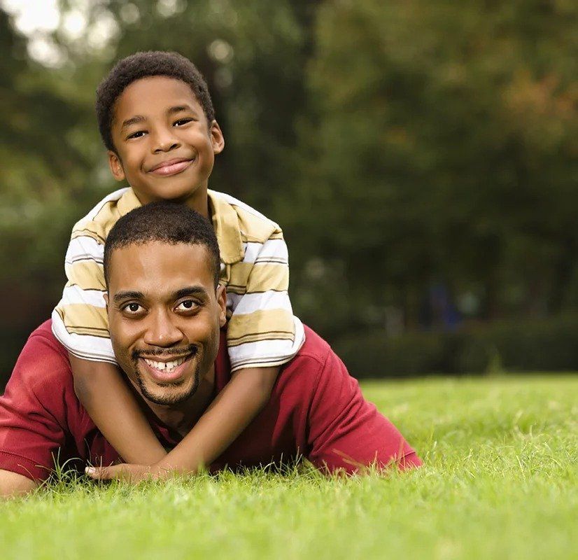 A boy is laying on a man 's shoulders in the grass