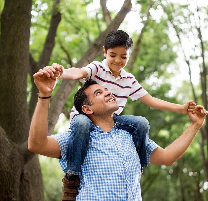 A man is carrying a boy on his shoulders in the woods.