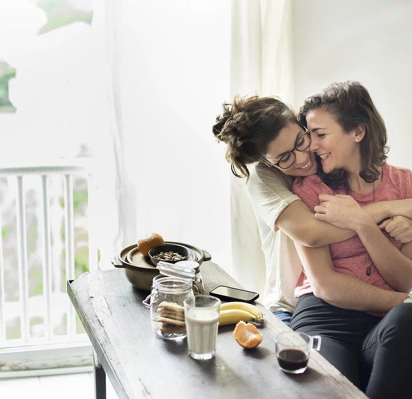 Two women are hugging each other while sitting at a table.