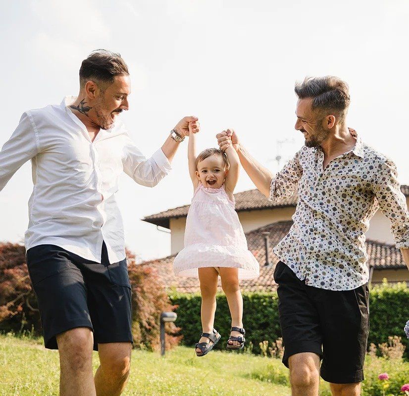 Two men are holding a little girl in their arms in a field.