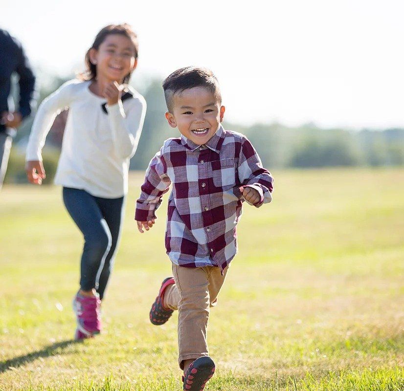 A boy and a girl are running in a field.