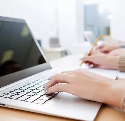 A person is typing on a laptop computer while holding a pencil.