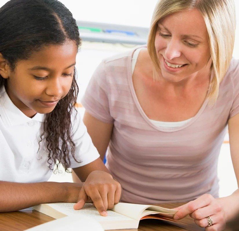 A woman is helping a young girl read a book