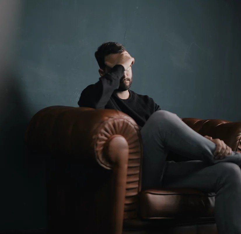 A man is sitting on a couch covering his face with his hand.