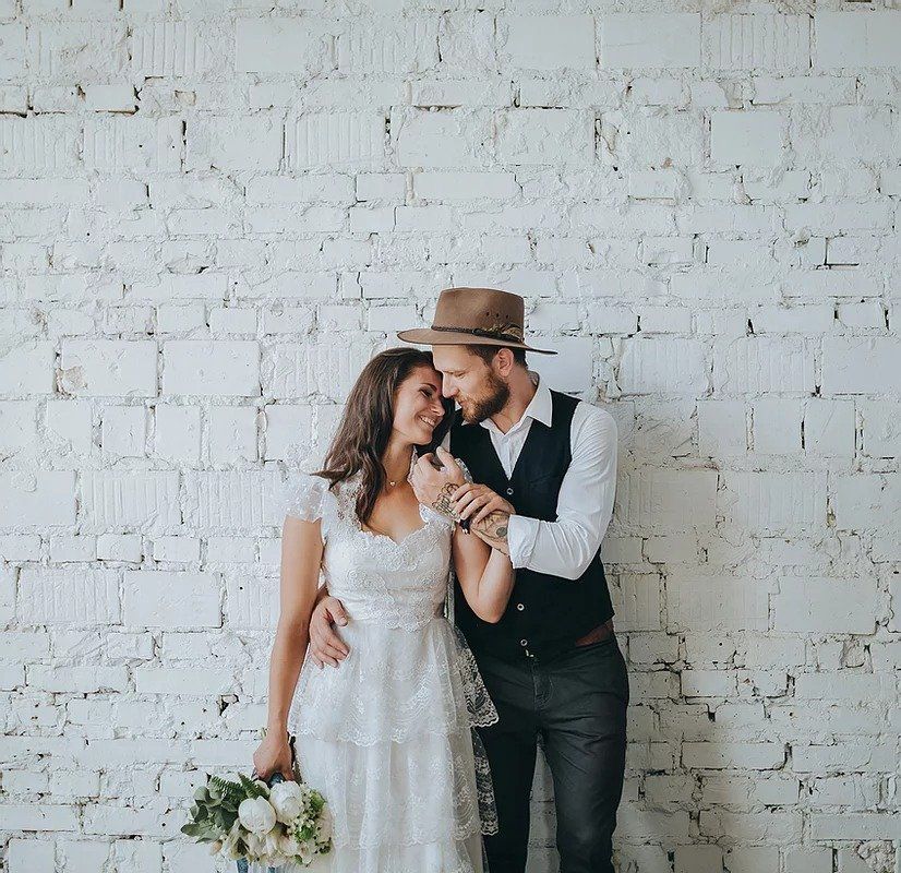 A bride and groom are posing for a picture in front of a white brick wall.