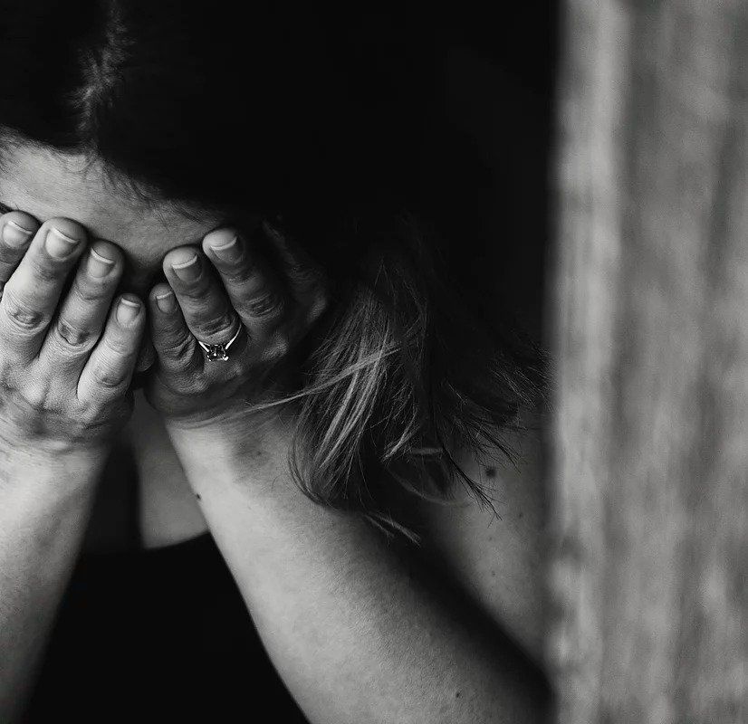 A woman is covering her face with her hands in a black and white photo.