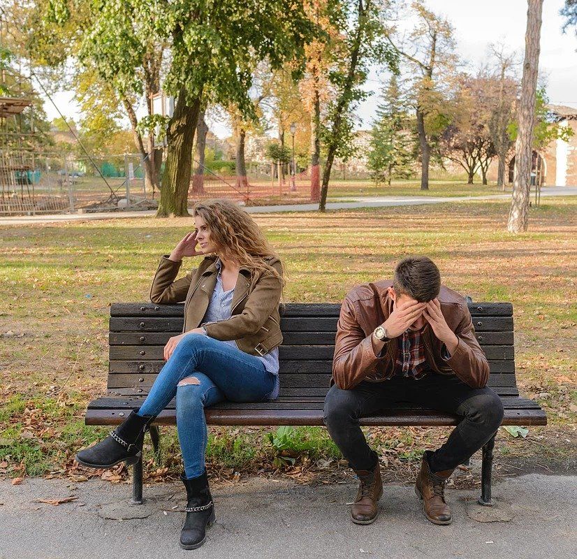 A man and a woman are sitting on a bench in a park.