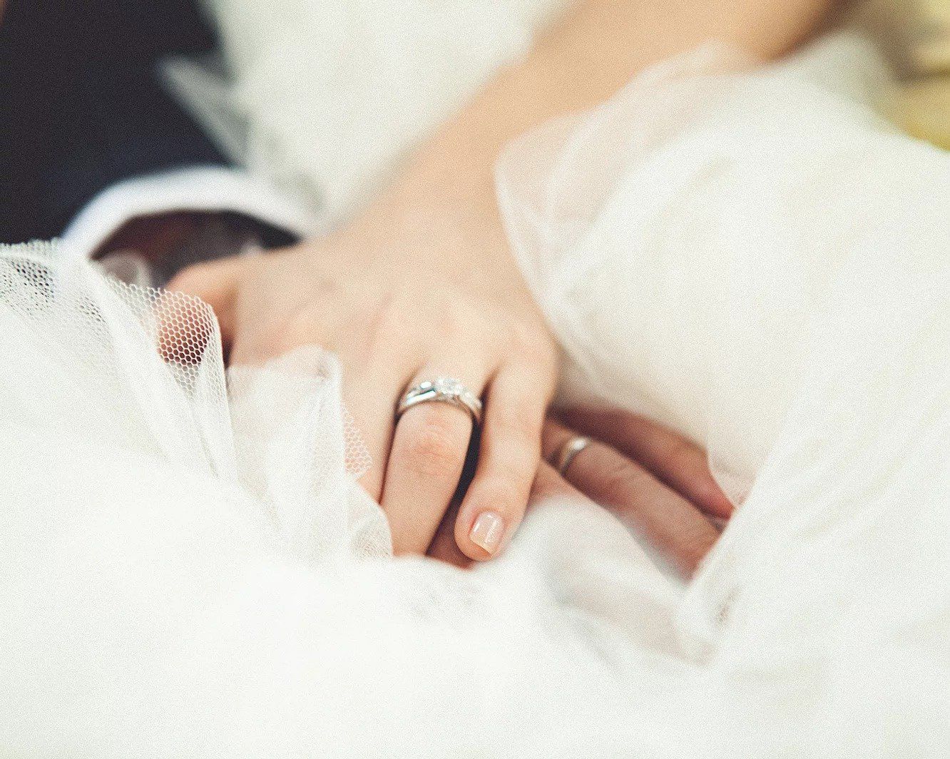A bride and groom are holding hands with their wedding rings on their fingers.
