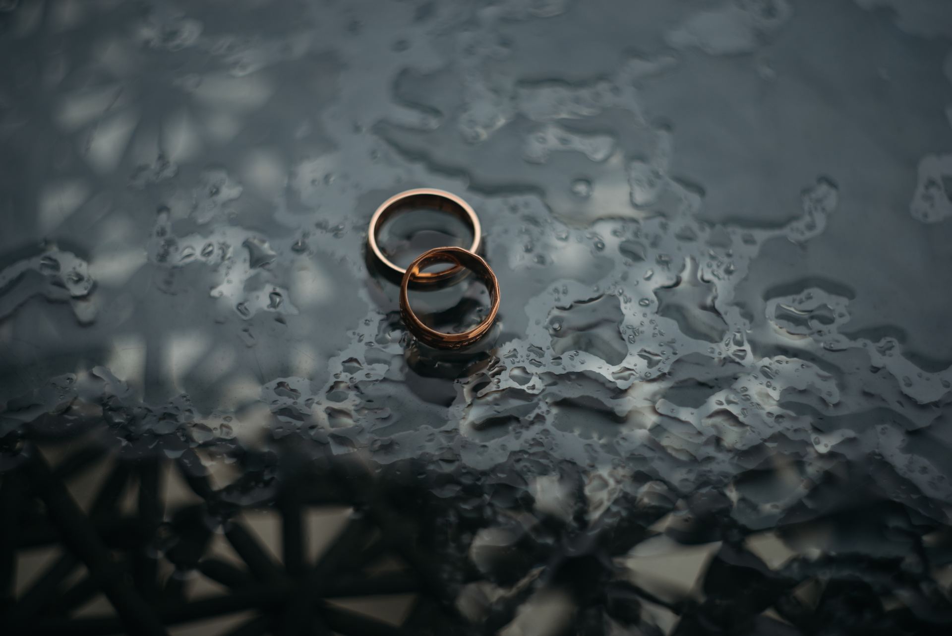Two wedding rings are sitting on a wet surface.