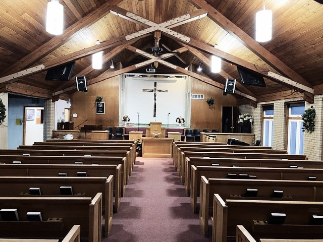 Empty church sanctuary with wooden pews, vaulted timber ceiling, and a cross on the front wall