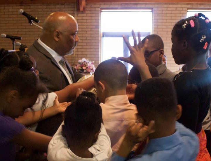 People gathered indoors around a speaker, one person raising a hand near a microphone stand.
