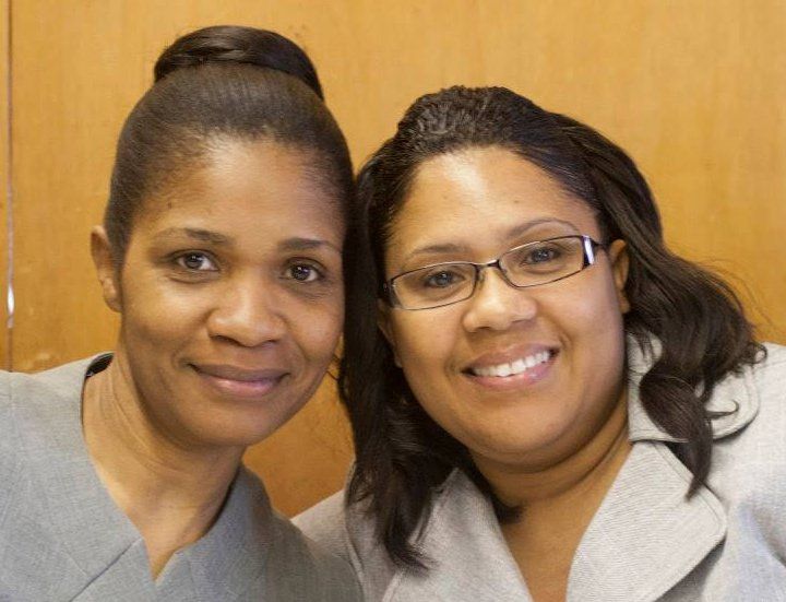 Two smiling women posing together against a warm wood-paneled background