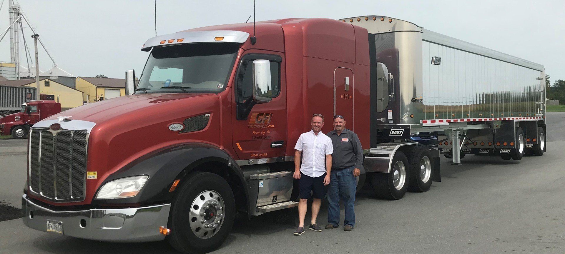 Two men are standing in front of a large red semi truck.