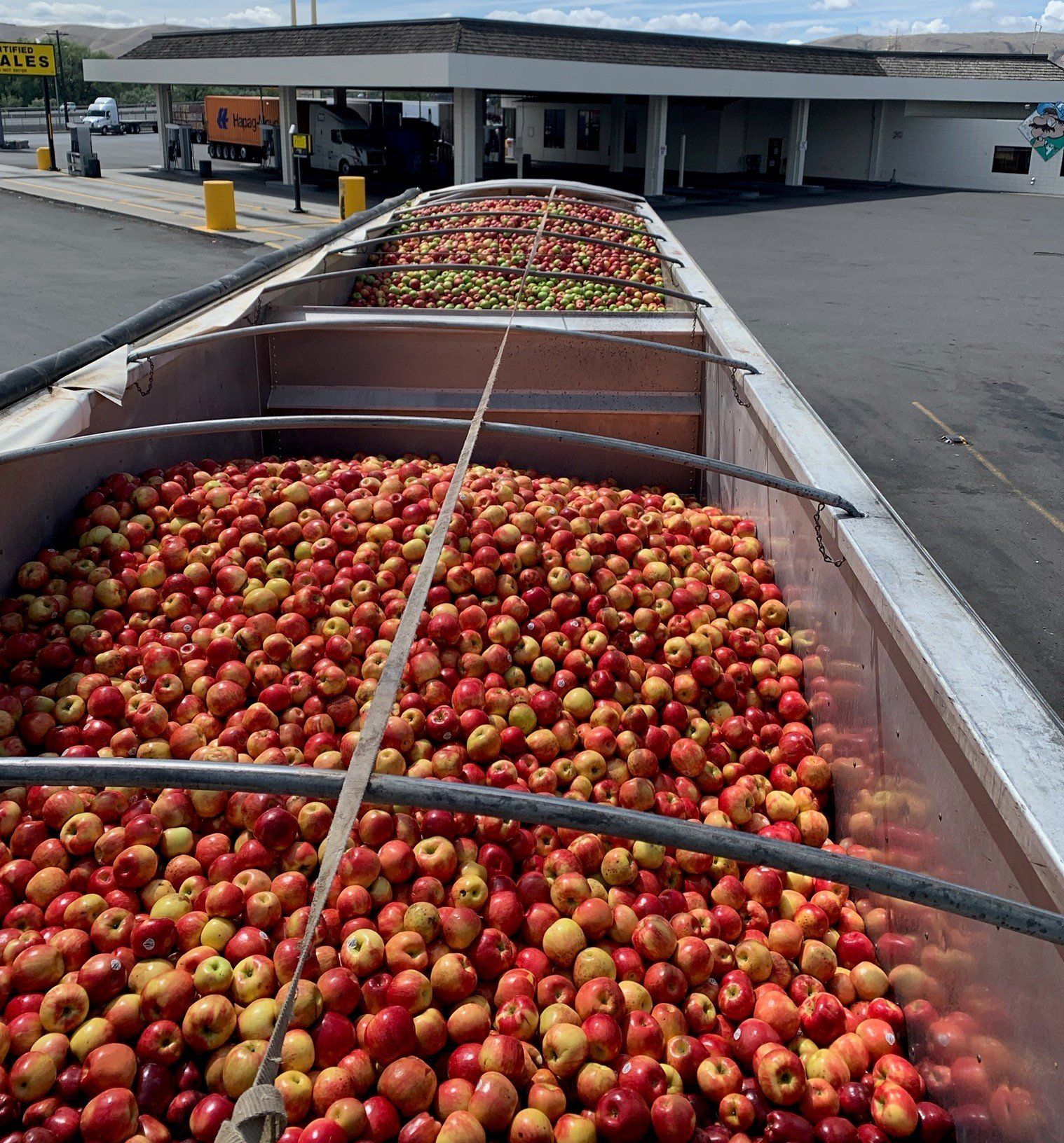 a truck full of apples is parked in front of a gas station