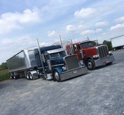 two semi trucks are parked next to each other in a gravel lot .