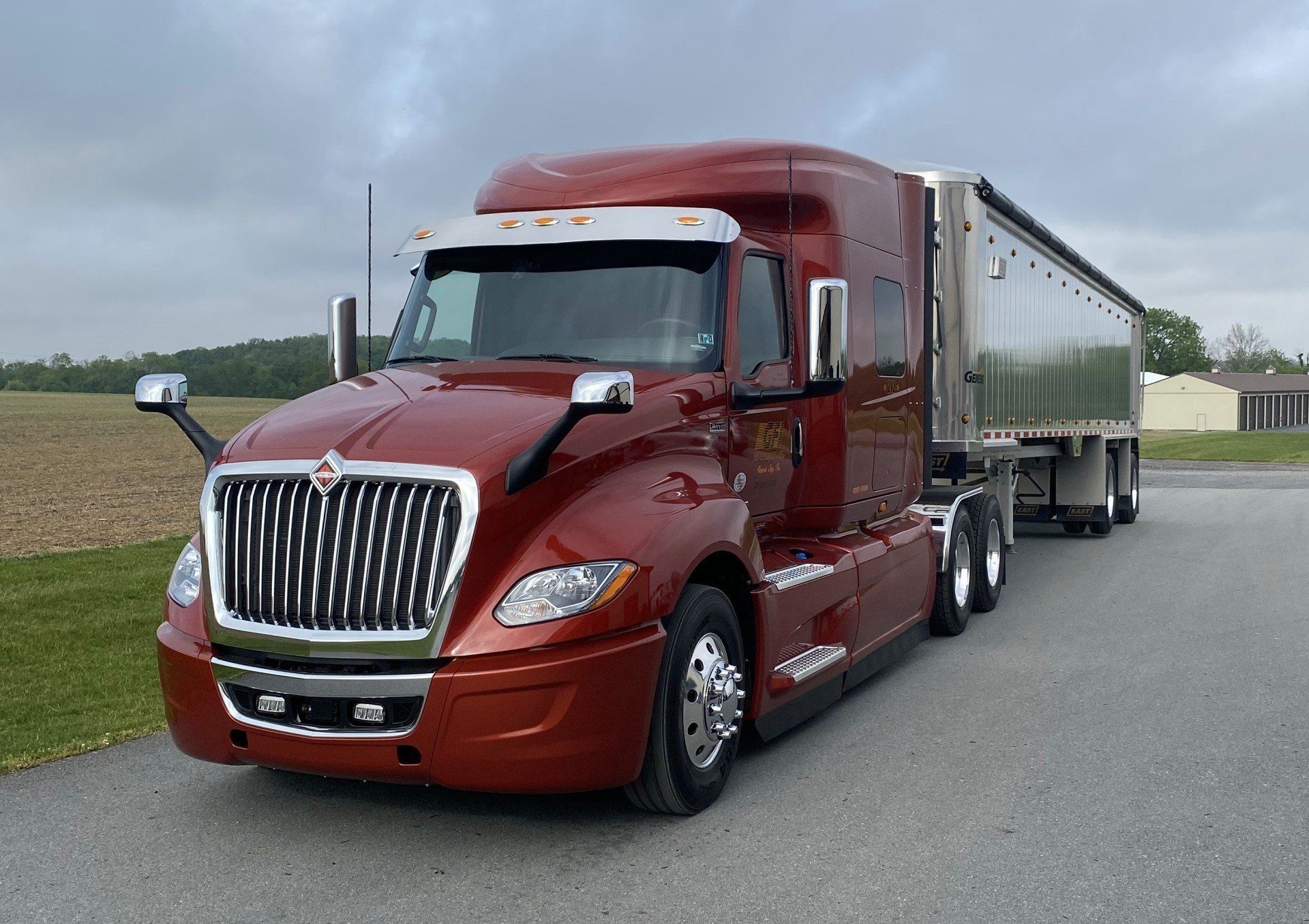 A red semi truck is parked on the side of the road next to a field.