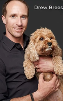 Drew brees is holding a small brown dog in his arms