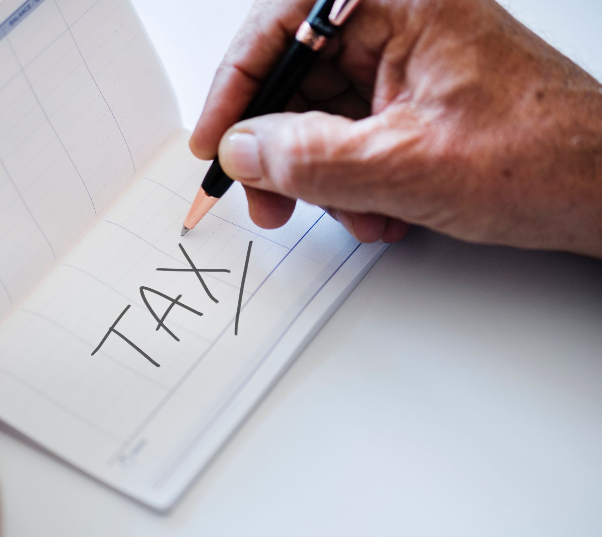 A person is writing the word tax on a piece of paper