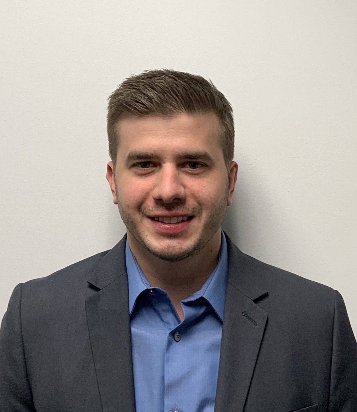 A man in a suit and blue shirt is smiling for the camera.