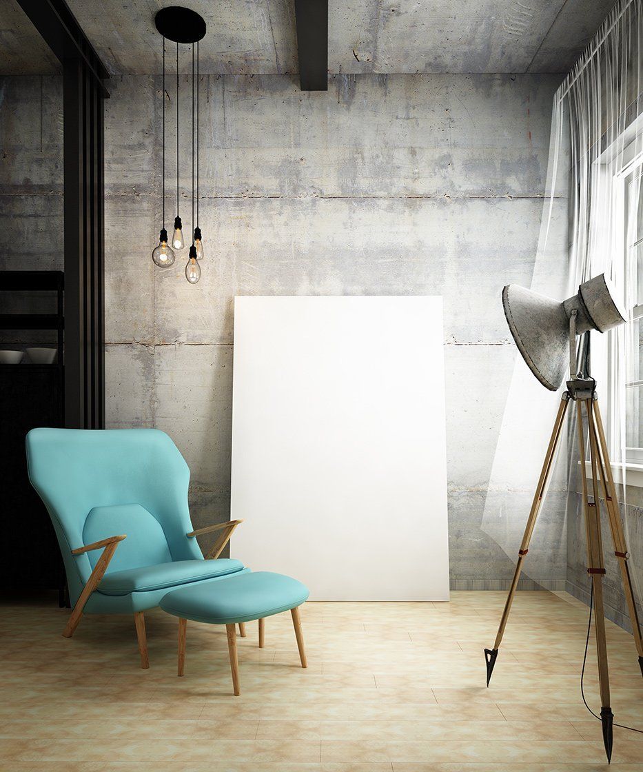 A turquoise armchair and ottoman sit before a large, blank white poster against a grey concrete wall in a minimalist room.