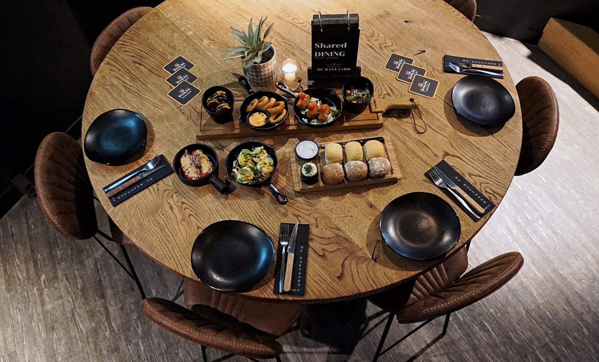 Impressie shared dining van een ronde tafel gedekt met eten, drinken en borden in een eetruimte met warme tinten.