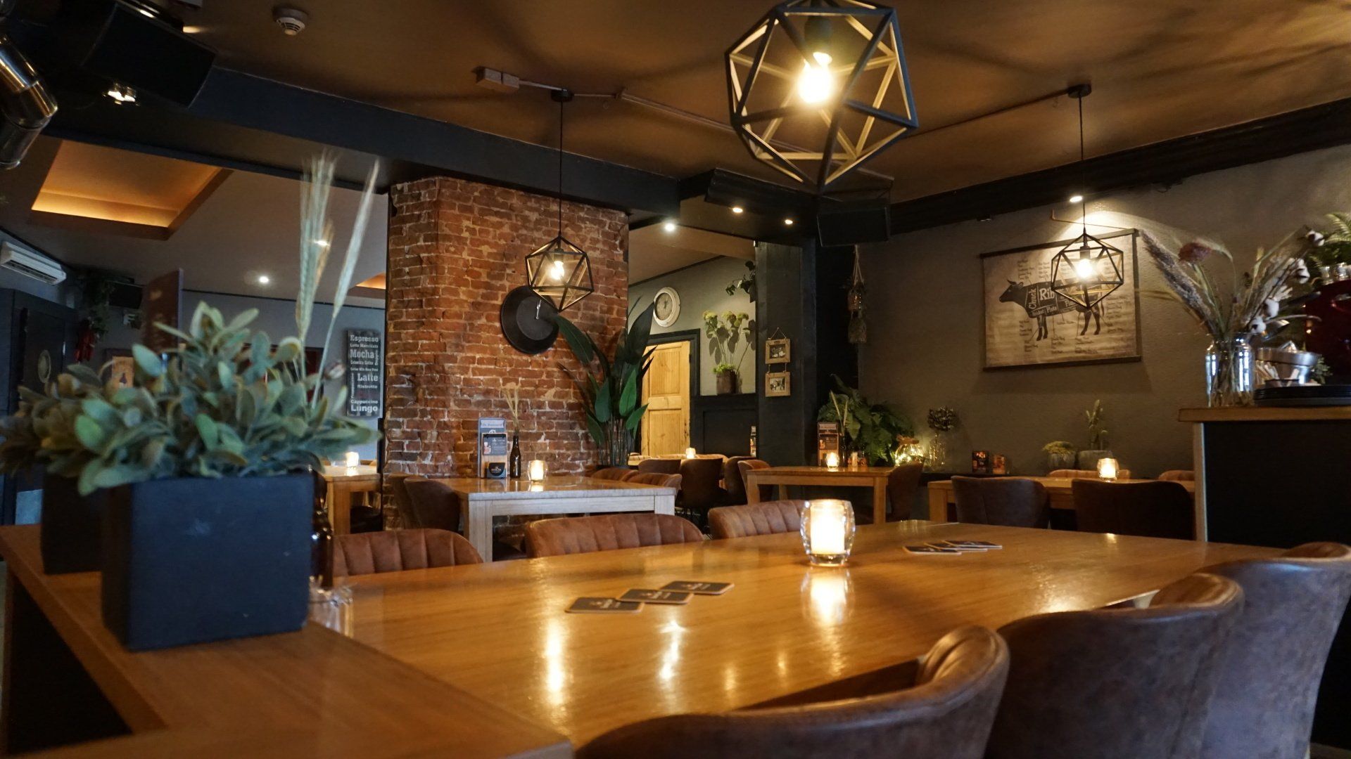 Een warme, stijlvolle lounge met houten tafels, een bakstenen open haard, hanglampen en gestoffeerde stoelen.